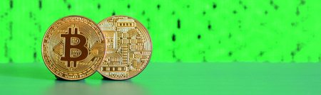 Two gold bitcoins lie on the green surface on the background of the display, which shows the process of mining the crypto currencyの写真素材