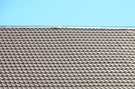 A fragment of a roof from a metal tile of dark red color. Quality Roofing