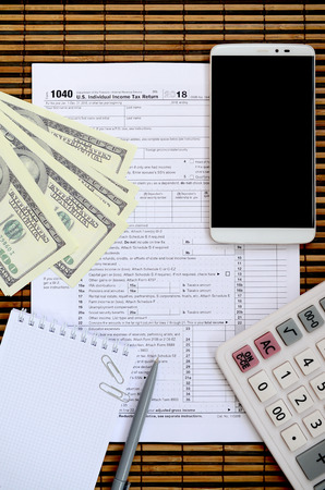 Composition of items lying on the 1040 tax form. Dollar bills, pen, calculator, smartphone, paper clip and notepad. The time to pay taxesの写真素材