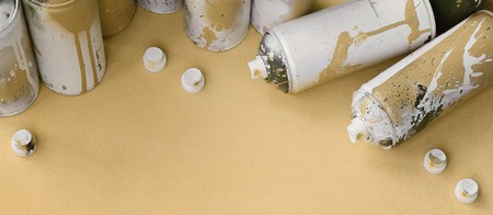 Some used orange aerosol spray cans and nozzles with paint drips lies on a blanket of soft and furry light orange fleece fabric. Classic fashion design color. Graffiti hooliganism conceptの写真素材