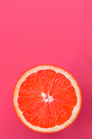 Top view of an one grapefruit slice on bright background in pink color. A saturated citrus texture imageの写真素材
