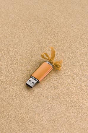 Orange usb flash memory card with a blue bow lies on a blanket of soft and furry light orange fleece...