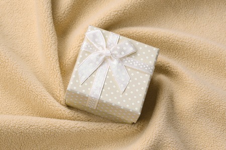 A small gift box in orange with a small bow lies on a blanket of soft and furry light orange fleece fabric with a lot of relief folds. Packing for a gift to your lovely girlfriendの写真素材