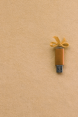 Orange usb flash memory card with a blue bow lies on a blanket of soft and furry light orange fleece...