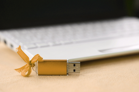 Orange usb flash memory card with a bow lies on a blanket of soft and furry orange fleece fabric beside to a white laptop. Classic female gift design for a memory cardの写真素材