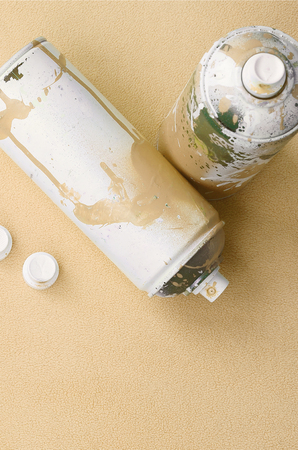 Some used orange aerosol spray cans and nozzles with paint drips lies on a blanket of soft and furry light orange fleece fabric. Classic fashion design color. Graffiti hooliganism conceptの写真素材