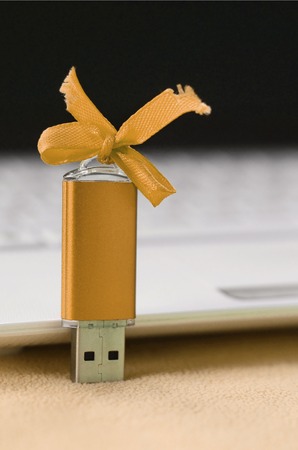 Orange usb flash memory card with a bow lies on a blanket of soft and furry light orange fleece fabric beside to a white laptop. Classic female gift design for a memory cardの写真素材
