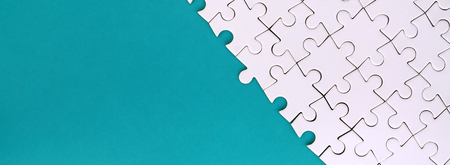 Fragment of a folded white jigsaw puzzle on the background of a blue plastic surface. Texture photo with copy space for textの写真素材