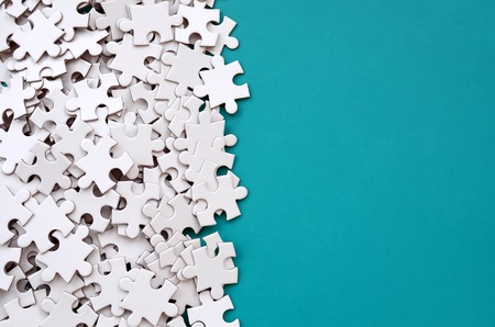 A pile of uncombed elements of a white jigsaw puzzle lies on the background of a blue surface. Texture photo with copy space for textの写真素材