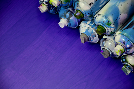 Still life with a large number of used colorful spray cans of aerosol paint lying on the treated wooden surface in the artist's graffiti workshop. Dirty and stained cans for spray artの写真素材