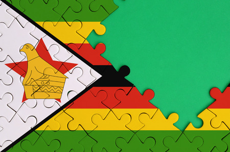 Zimbabwe flag  is depicted on a completed jigsaw puzzle with free green copy space on the right side.の写真素材