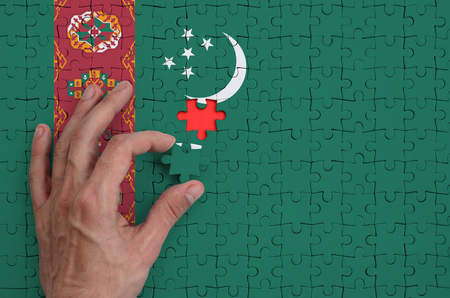 Turkmenistan flag  is depicted on a puzzle, which the man's hand completes to fold.の写真素材
