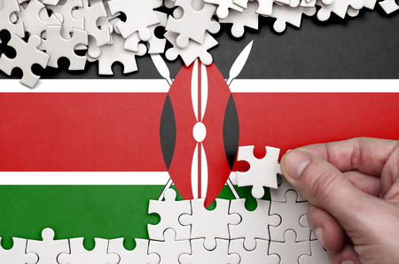 Kenya flag  is depicted on a table on which the human hand folds a puzzle of white color.の写真素材