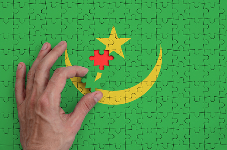 Mauritania flag  is depicted on a puzzle, which the man's hand completes to fold.の写真素材