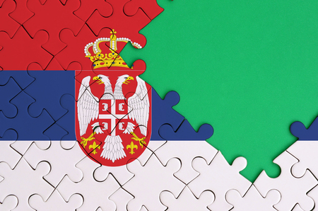 Serbia flag  is depicted on a completed jigsaw puzzle with free green copy space on the right side.の写真素材
