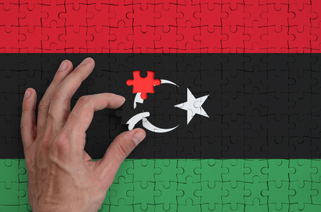 Libya flag  is depicted on a puzzle, which the man's hand completes to fold.の写真素材