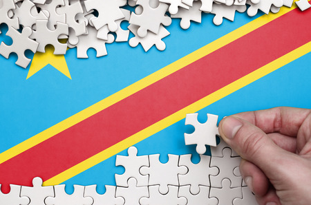 Democratic Republic of the Congo flag  is depicted on a table on which the human hand folds a puzzle of white color.の写真素材