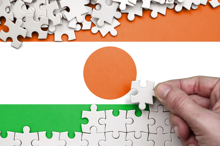 Niger flag  is depicted on a table on which the human hand folds a puzzle of white color.の写真素材