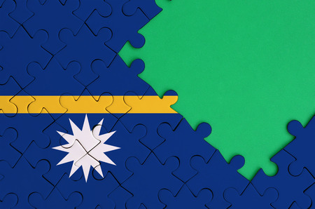 Nauru flag  is depicted on a completed jigsaw puzzle with free green copy space on the right side.の写真素材