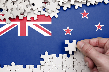 New Zealand flag  is depicted on a table on which the human hand folds a puzzle of white color.の写真素材