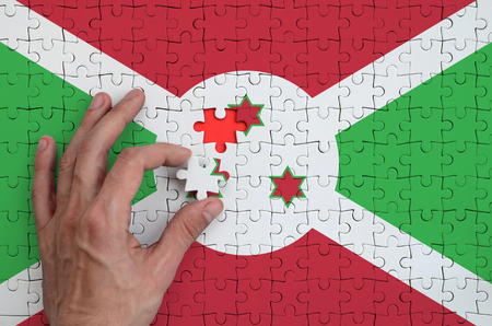 Burundi flag  is depicted on a puzzle, which the man's hand completes to fold.の写真素材