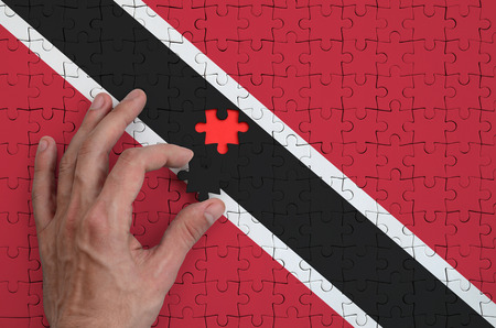 Trinidad and Tobago flag  is depicted on a puzzle, which the man's hand completes to fold.の写真素材