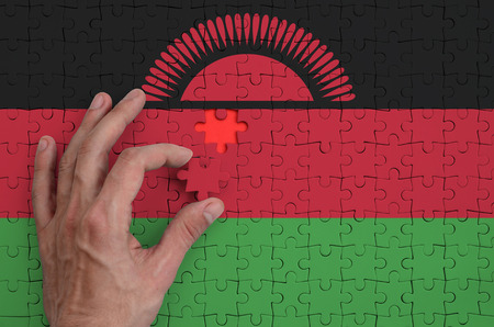 Malawi flag  is depicted on a puzzle, which the man's hand completes to fold.の写真素材