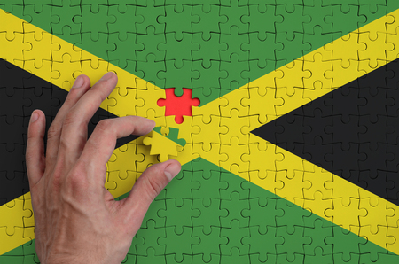 Jamaica flag  is depicted on a puzzle, which the man's hand completes to fold.の写真素材