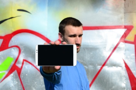 The graffiti artist demonstrates a smartphone with an empty black screen against the background of a...