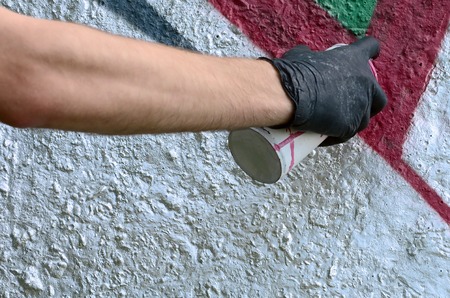 A hand in black gloves paints graffiti on a concrete wall. Illegal vandalism concept. Street art.の写真素材
