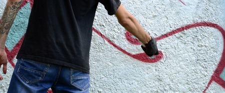 A young hooligan paints graffiti on a concrete wall. Illegal vandalism concept. Street art.の写真素材