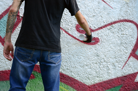 A young hooligan paints graffiti on a concrete wall. Illegal vandalism concept. Street art.の写真素材