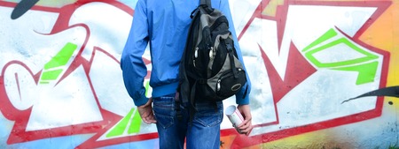 A young graffiti artist with a black bag looks at the wall with his graffiti on a wall. Street art concept.の写真素材