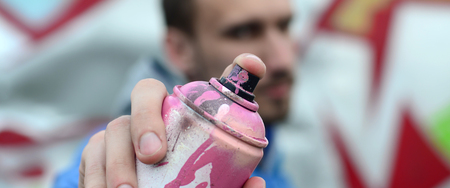A young graffiti artist in a blue jacket is holding a can of paint in front of him against a...