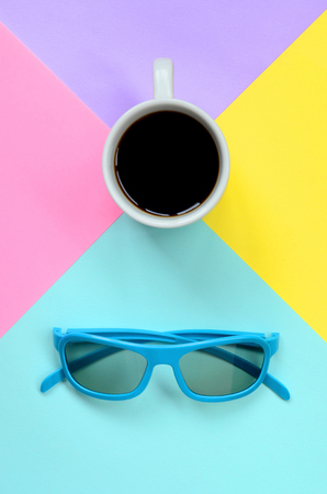 Small white coffee cup and blue sunglasses on texture background of fashion pastel blue, yellow, violet and pink colors paper in minimal concept.の写真素材