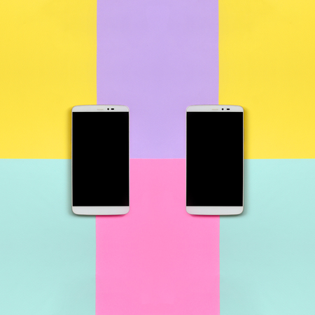 Two modern smartphones with black screens on texture background of fashion pastel blue, yellow, violet and pink colors paper in minimal concept.の写真素材