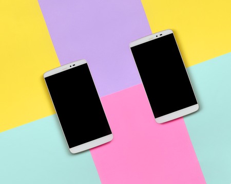 Two modern smartphones with black screens on texture background of fashion pastel blue, yellow, violet and pink colors paper in minimal concept.の写真素材