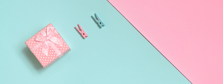 Small pink gift box and two pegs lie on texture background of fashion pastel blue and pink colors paper in minimal concept.の写真素材