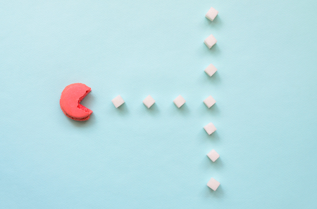A composition of macaroon with an open mouth that is going to eat sugar cubes on a blue pastel background. The concept of old video games.の写真素材