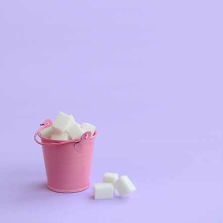 A miniature pink bucket filled with cubes of sugar lies on a purple pastel background. Minimal concept.の写真素材