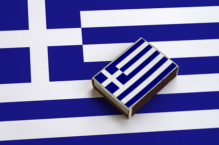 Greece flag  is pictured on a matchbox that lies on a large flag.