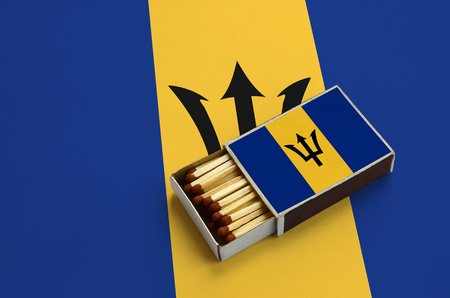 Barbados flag  is shown in an open matchbox, which is filled with matches and lies on a large flag.の写真素材