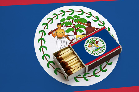Belize flag  is shown in an open matchbox, which is filled with matches and lies on a large flag.の写真素材