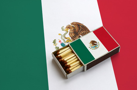 Mexico flag  is shown in an open matchbox, which is filled with matches and lies on a large flag.の写真素材