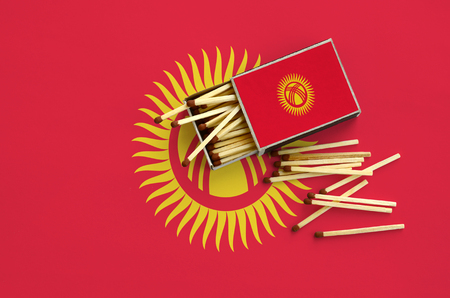 Kyrgyzstan flag  is shown on an open matchbox, from which several matches fall and lies on a large flag.の写真素材
