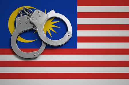 Malaysia flag  and police handcuffs. The concept of crime and offenses in the country.の写真素材