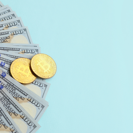 Golden bitcoins and hundred dollar bills lies on light blue background.