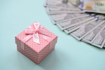 Pink dotted gift box lies near hundred dollar bills on a light blue background.の写真素材