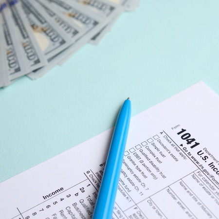 1041 tax form lies near hundred dollar bills and blue pen on a light blue background. US Income tax return for estates and trusts.の写真素材