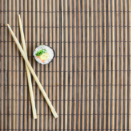 Sushi roll and wooden chopsticks lie on a bamboo straw serwing mat. Traditional Asian food. Top view. Flat lay minimalism shot with copy space.の写真素材